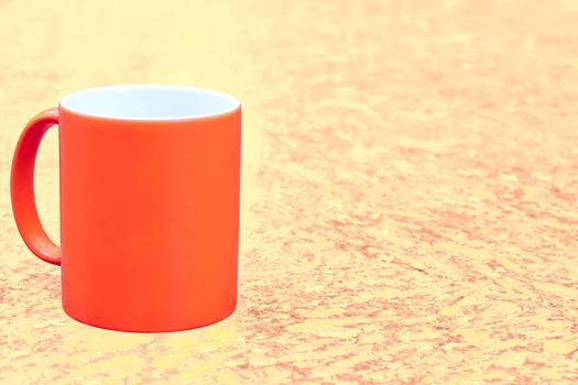 a small bowl-shaped container for drinking from, typically having a handle. Red ceramic cup mug on yellow brown spotted background. High quality photo