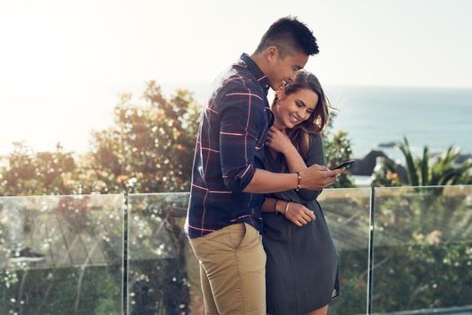 We love sharing our best moments online. an affectionate young couple using a cellphone together while relaxing outdoors