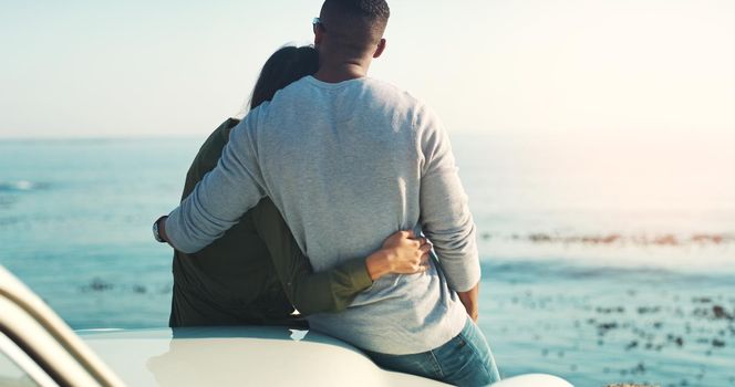 Embracing true love... Rearview shot of a young couple making a stop at the beach while out on a road trip