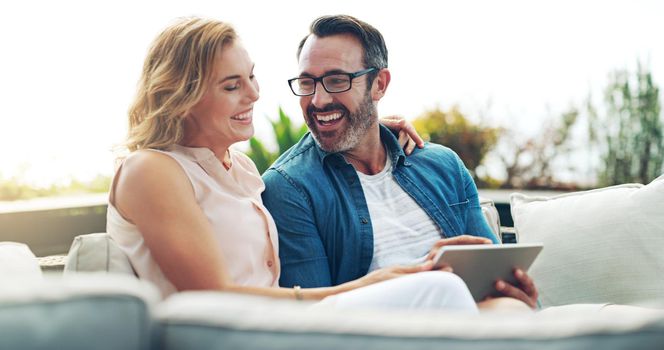 Sharing our fun with the world. an affectionate mature couple using a digital tablet while relaxing on a couch together outdoors