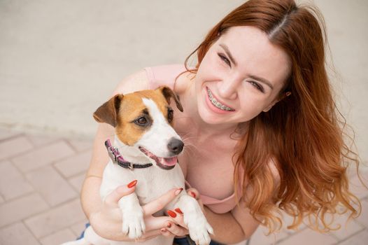 Young red-haired woman is cuddled with a jack russell terrier dog outdoors