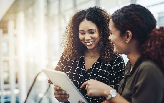 Our work will be so much easier with this tool. two attractive businesswomen using a digital tablet together while standing in a modern workplace