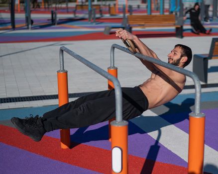 Shirtless man doing horizontal balance on parallel bars at sports ground