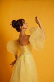 Profile portrait of a beautiful middle-aged woman in a yellow dress, her hair pulled up against a yellow background.