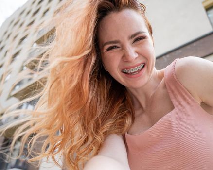 Beautiful young red-haired woman with braces on her teeth smiling in the summer outdoors.