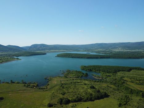 Aerial landscape from flying drone storage reservoir at mountain foot covered colorful spring forest. Beautiful view from above blue lake among highlands