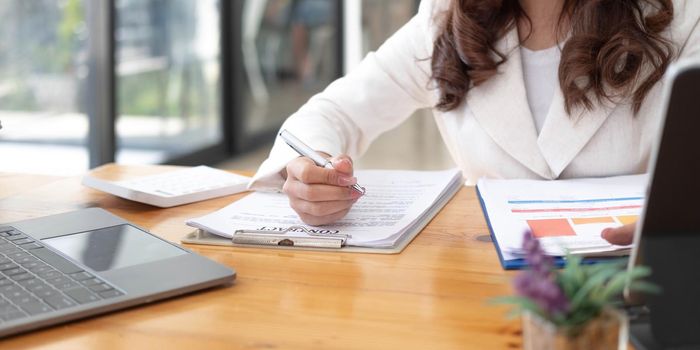 Business woman using calculator and laptop for do math finance on wooden desk in office and business working background, tax, accounting, statistics and analytic research concept.