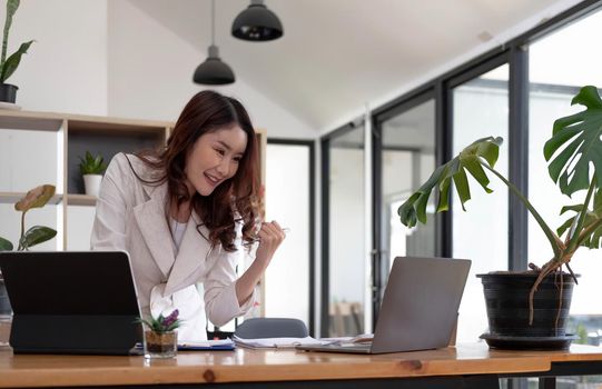 Excited executive receiving good news online sitting in a coffee shop, Business Success. Asian Businesswoman Celebrating Victory At Work. Free Space.