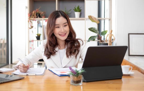 Beautiful Asian businesswoman analyzes charts using laptop calculator at the office..