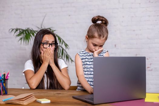 Irritated mother watching at the mistakes her daughter's homework on a laptop. Emotions.