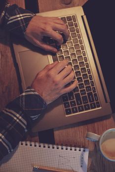 Young man drinking coffee in cafe and using laptop. Man's hands using laptop during coffee break. Working from cafe concept