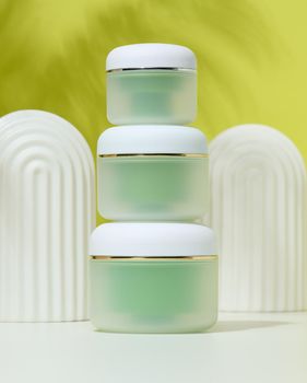 Green jar for cosmetics on a white table. Packaging for cream, gel, serum, advertising and product promotion