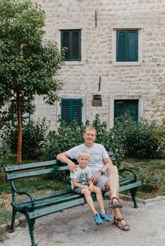 Father and son sitting on wooden bench outdoors. Father and son sitting on bench in park, men talks, spending time together