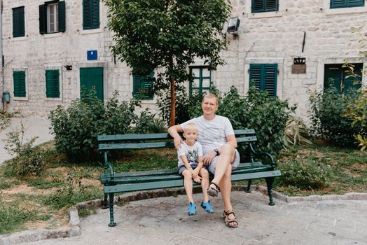 Father and son sitting on wooden bench outdoors. Father and son sitting on bench in park, men talks, spending time together