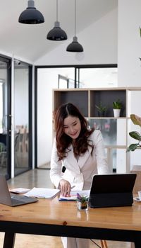 Asian Businesswoman Using laptop computer and working at office with calculator document on desk, doing planning analyzing the financial report, business plan investment, finance analysis concept..