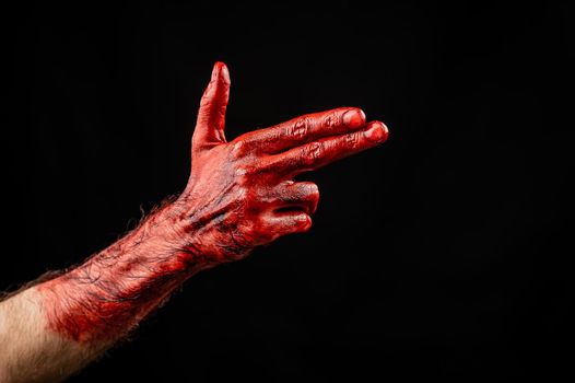 Bloody male hand gesturing shows a gun against black background