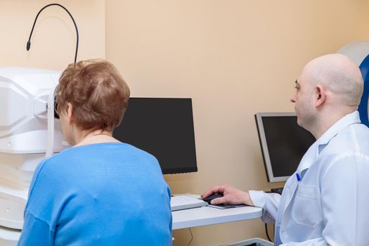 A male ophthalmologist checks the eyesight of an adult woman using a modern device.