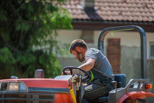 A man on a mini-excavator levels a piece of land, loosens the soil
