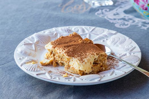 Tiramisu cake in a white plate on the table with a spoon.