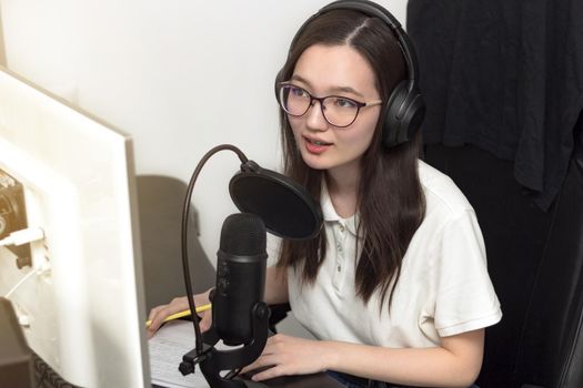 Young millennial woman with glasses, professional microphone and headphones recording podcast at studio, technology and media concept