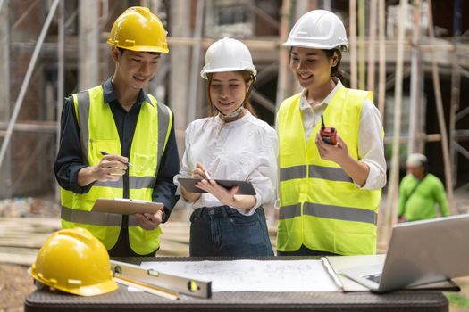 architector and engineers with draft plan of building and tablet computer talking on constructing site