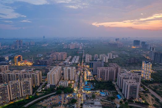 drone aerial shot showing busy traffic filled streets between skyscrapers filled with houses, homes and offices with a red sunset sky showing the hustle and bustle of life in Gurgaon, delhi drone shot