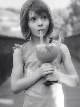 Funny little girl drinking mixed berries and citrus juice outdoors