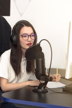 Young millennial woman with glasses, professional microphone and headphones recording podcast at studio, technology and media concept, vertikal image