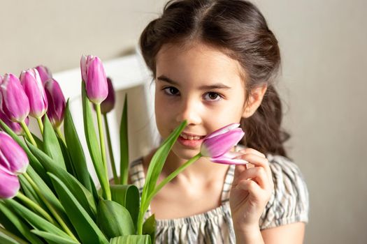 Portrait of a beautiful romantic little girl with a bouquet of purple tulips. Close up