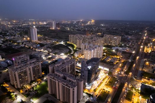 aerial drone shot showing brightly lit orange streets with skyscrapers, towers housing homes offices and shopping complexes in between with the city skyline in the distance in Gurgaon Delhi India drone shot