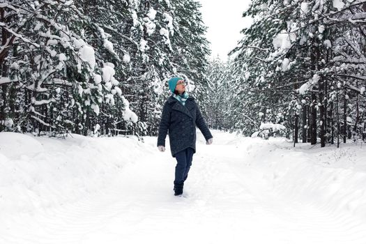 A woman walks through a beautiful winter snowy forest, looks at the trees.