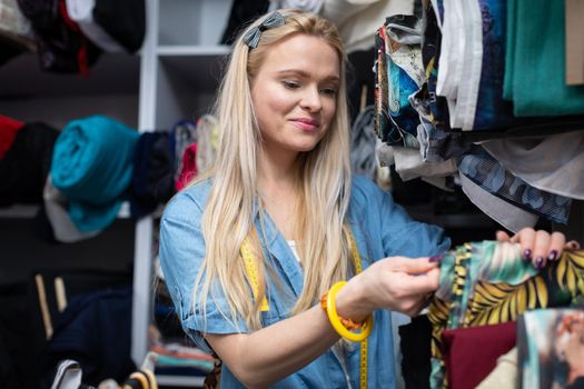 Tailor's shop with many different fabrics. A girl in a wholesale tailor's fabric shop. Blonde girl with long straight hair.