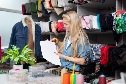 A young girl in a tailor's shop shapes a tailor's mold and adjusts it to fit the size of her next blouse. Blonde with long straight hair.