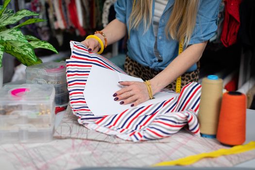 A clothing designer applies a tailor's blank to colored fabric and checks to see if it will fit and how it will look. A blonde woman with long straight hair.