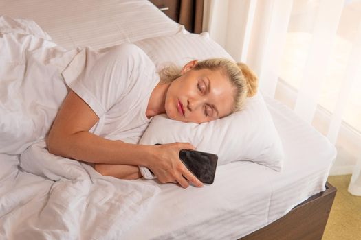 Woman blonde mobile sleep phone beautiful bed blanket view bedroom, from female pillow in people and smile attractive, comfortable healthy. Indoors serene day,