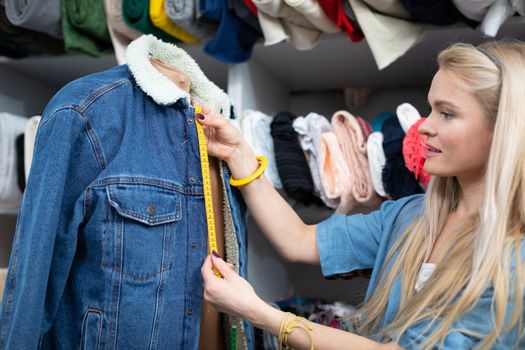 A clothing designer measures the exact parts in a denim jacket to be replaced with new ones. A girl with light skin complexion.
