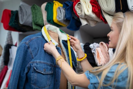 A clothing designer measures the exact parts in a denim jacket to be replaced with new ones. A girl with light skin complexion.