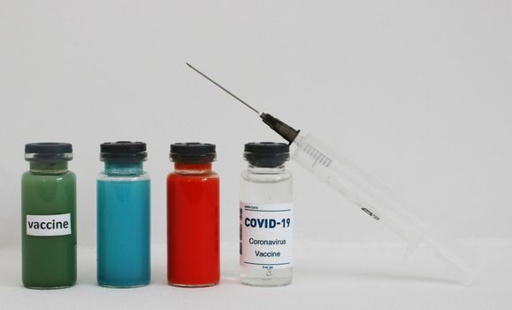 Four ampoules with vaccine and medicines and a syringe on a light background.