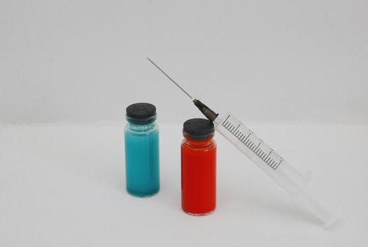 Red and blue medicine bottle and disposable injection syringe. Two ampoules with covid-19 vaccine and a syringe on a white background.