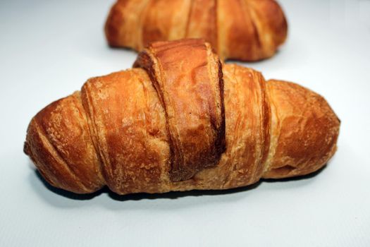 Fresh crispy croissant close-up on a light background. Blurred croissant in the background. Cooking, home baking.