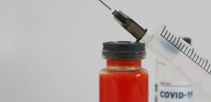 Two ampoules with covid-19 vaccine and a syringe on a white background.