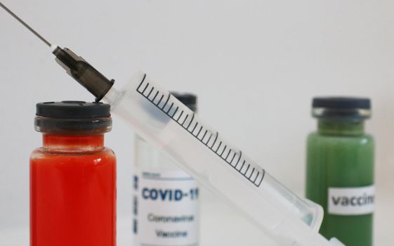 One ampoule with covid vaccine, blue and red ampoule with medicine to strengthen immunity. Three multi-colored ampoules with medicine and a syringe on a light gray background.