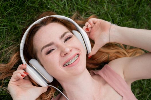 A young red-haired woman lies on the grass and listens to music