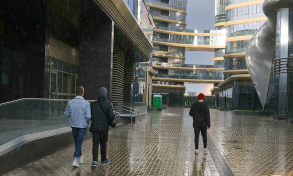 Walking people on the background of skyscrapers in the rain. Glare on glass.