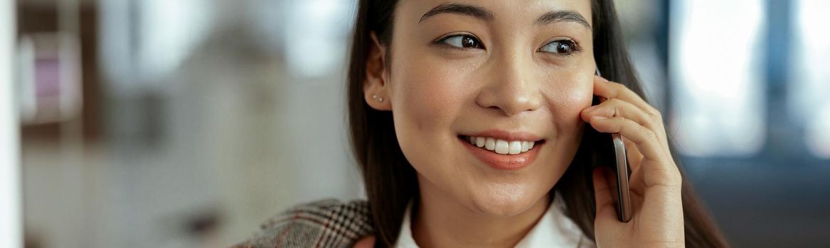 Close up of smiling asian business woman making phone call standing at office. High quality photo