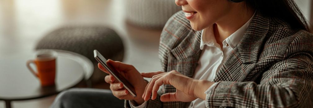 Smiling asian business woman listening music on headphones sitting in cozy cafe. High quality photo