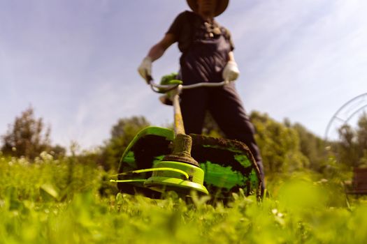 A young man is actively mowing a lawn with a lawn mower in his beautiful green floral summer garden, bottom view.