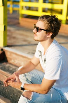 Young man in sunglasses sitting on the wooden steps. High quality photo