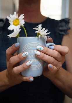 a young woman holds a blue cup of daisies, a beautiful summer manicure. High quality photo