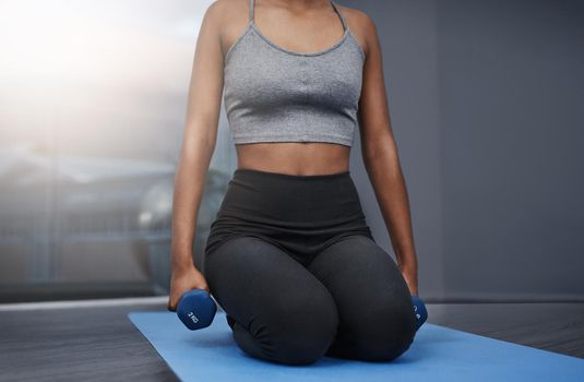 Composure is the hardest thing to maintain. an unrecognizable young woman on her knees holding dumbbells while exercising on her gym mat at home